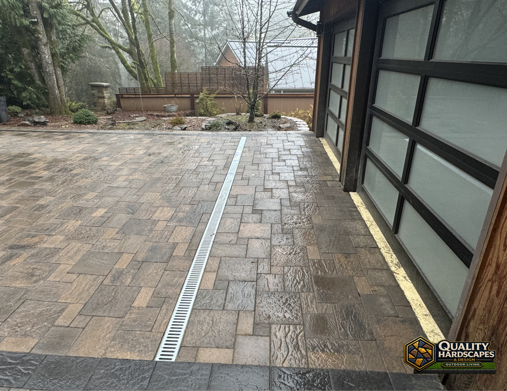 Backyard stone patio with a linear drainage channel beside a house wall and steps