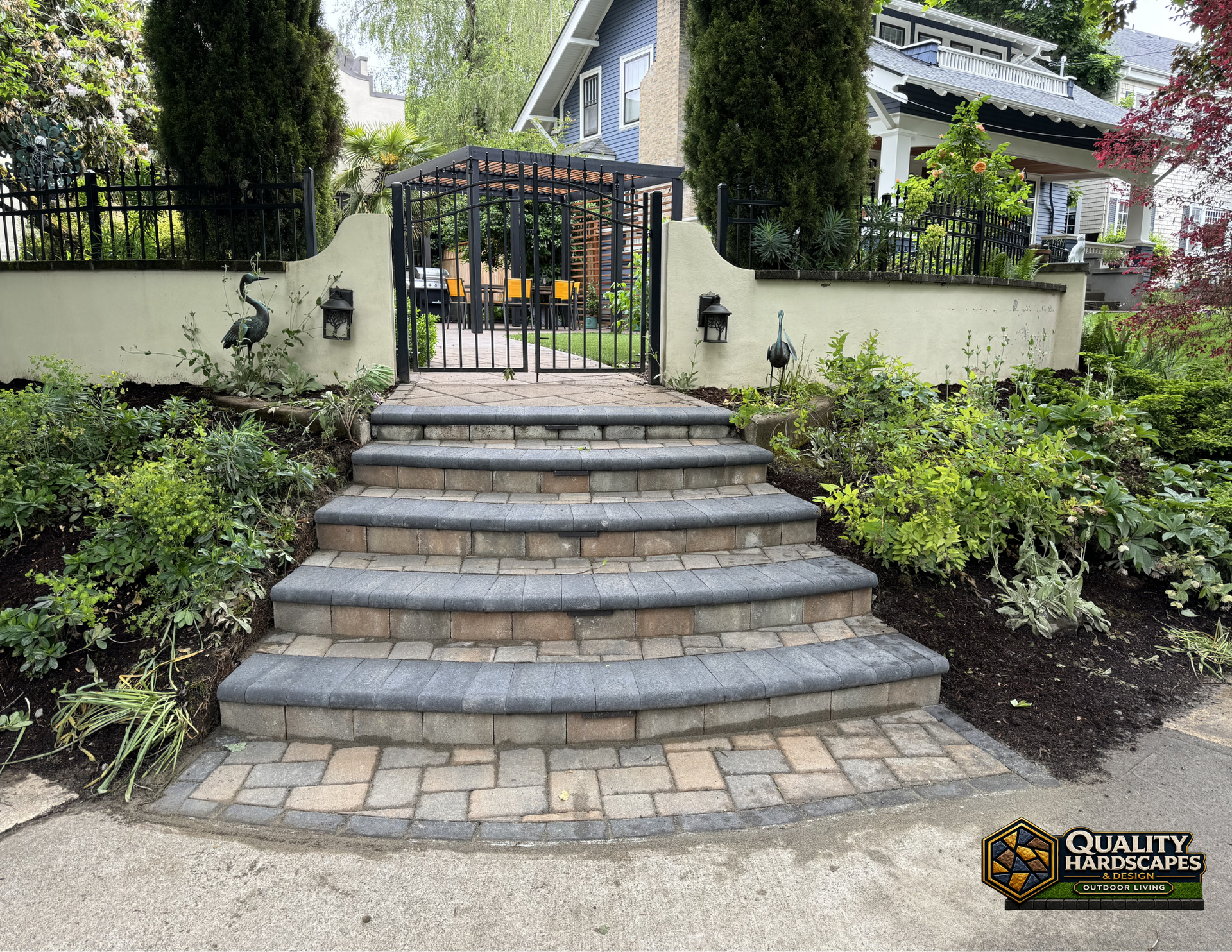 Stone steps lead to a gated garden entrance with black iron railings and lush landscaping.