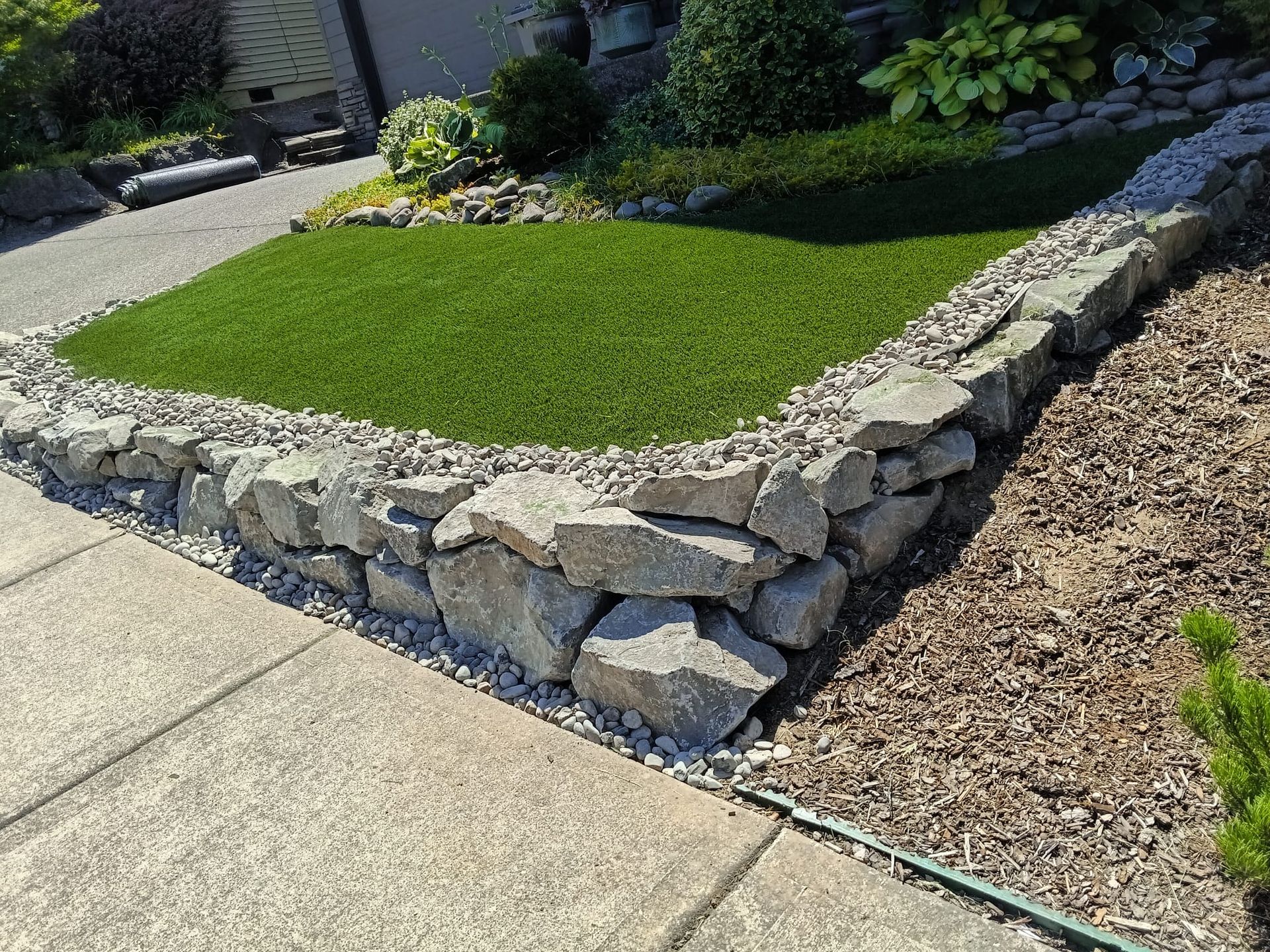 Stone retaining wall borders green turf in front yard.
