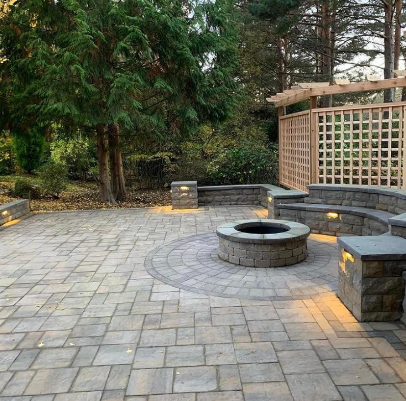 Stone patio with fire pit, built-in seating, and wooden trellis in a backyard setting.