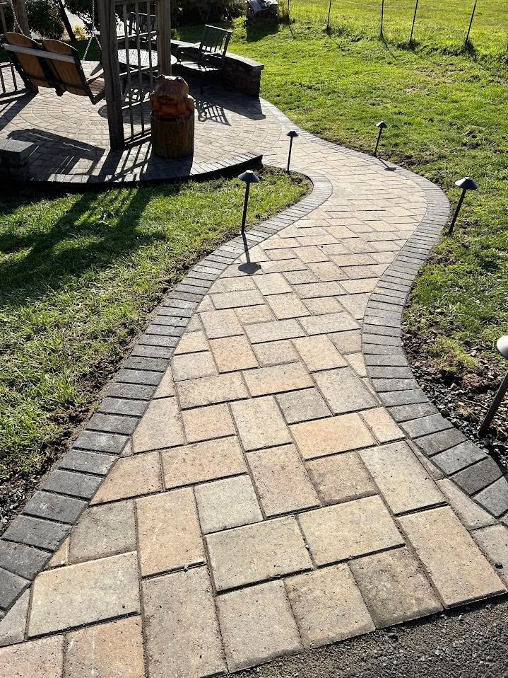 Brick pathway with dark border, lit by small lamps, curves through grass towards a gazebo.