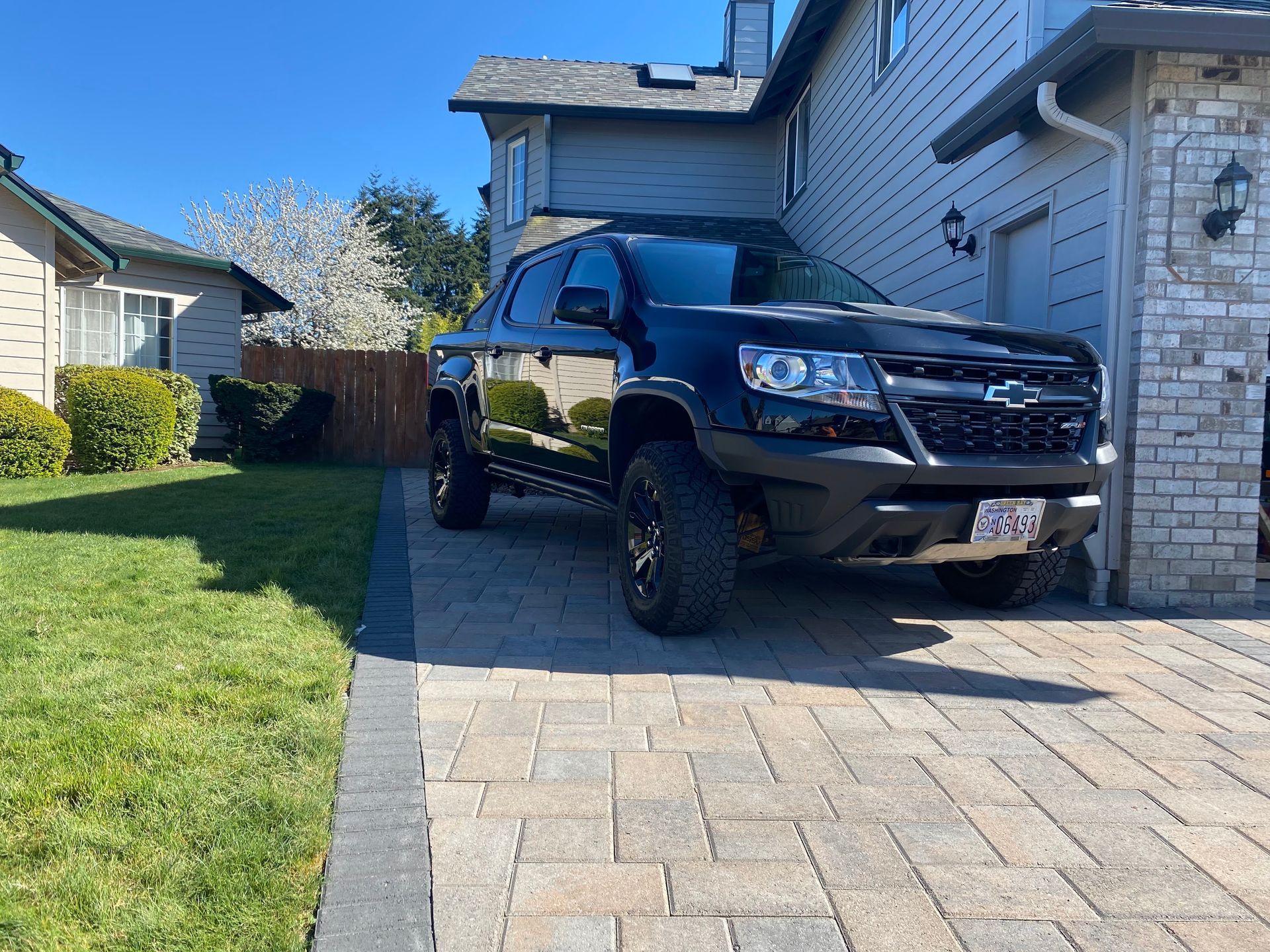 Black Chevrolet truck parked on a brick driveway beside a two-story house.