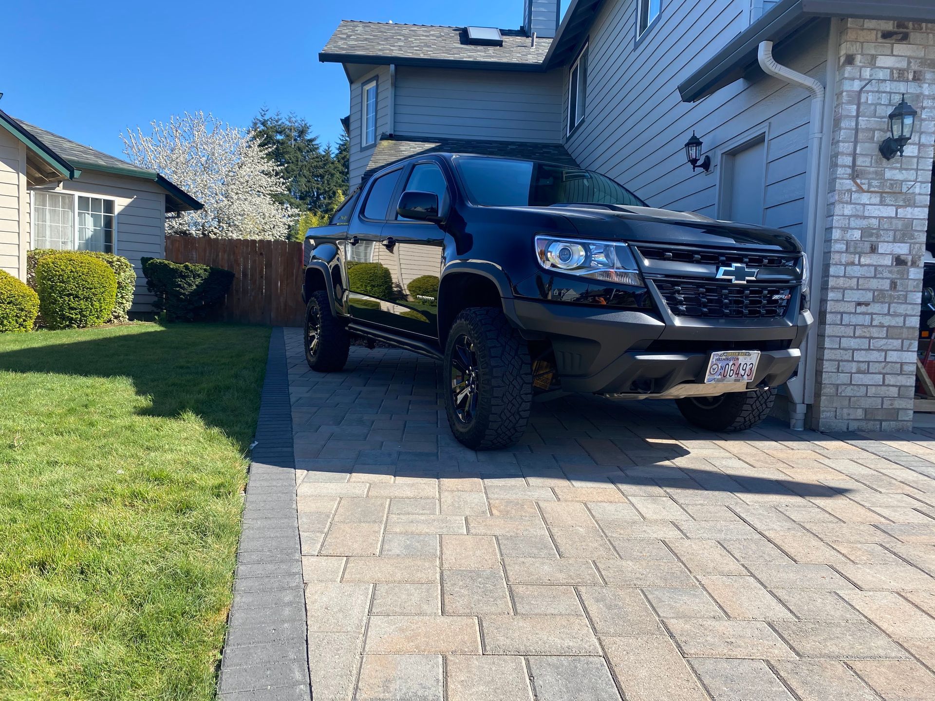 Dark blue pickup truck parked on a brick driveway in front of a house.
