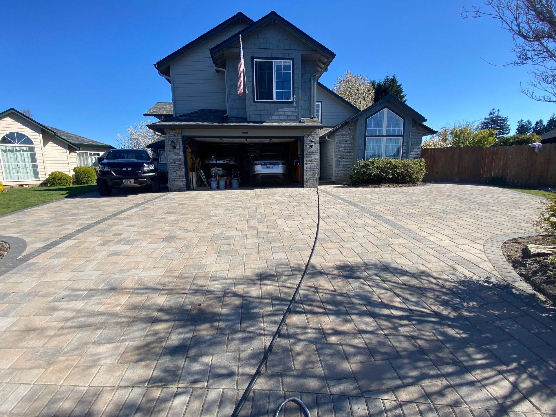 House with paver driveway and two-car garage. A car is parked inside the garage. Sunny day.