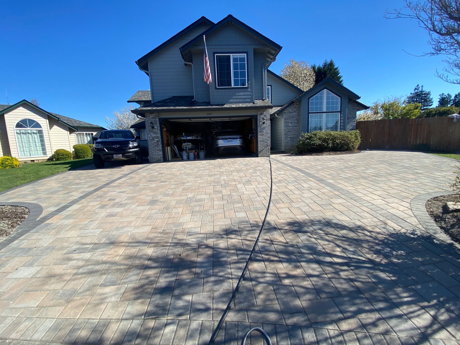 Paver driveway leading to a two-story house with an open garage. Blue sky.