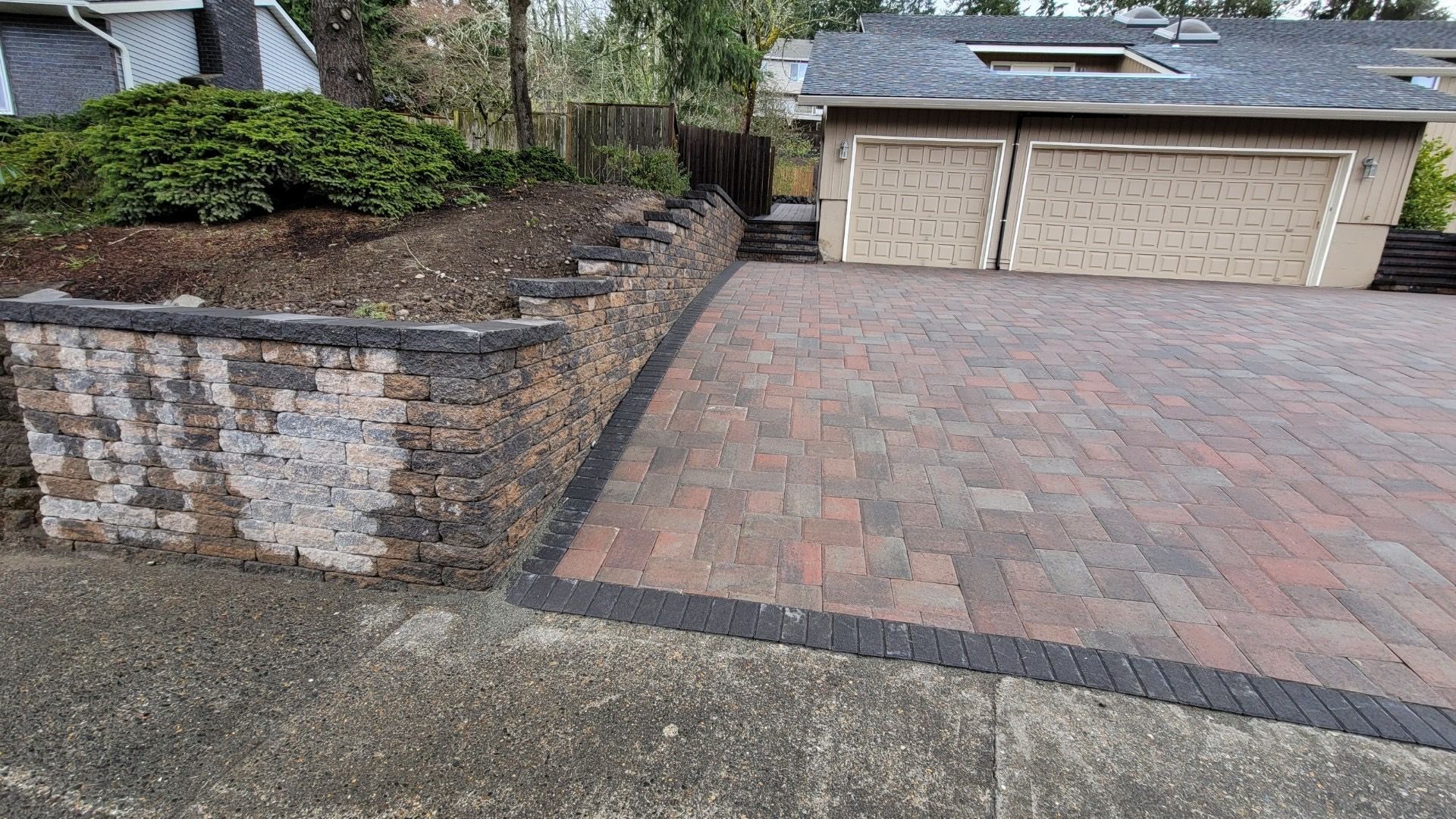 Brick driveway with retaining wall, garage, and landscaping in an outdoor setting.