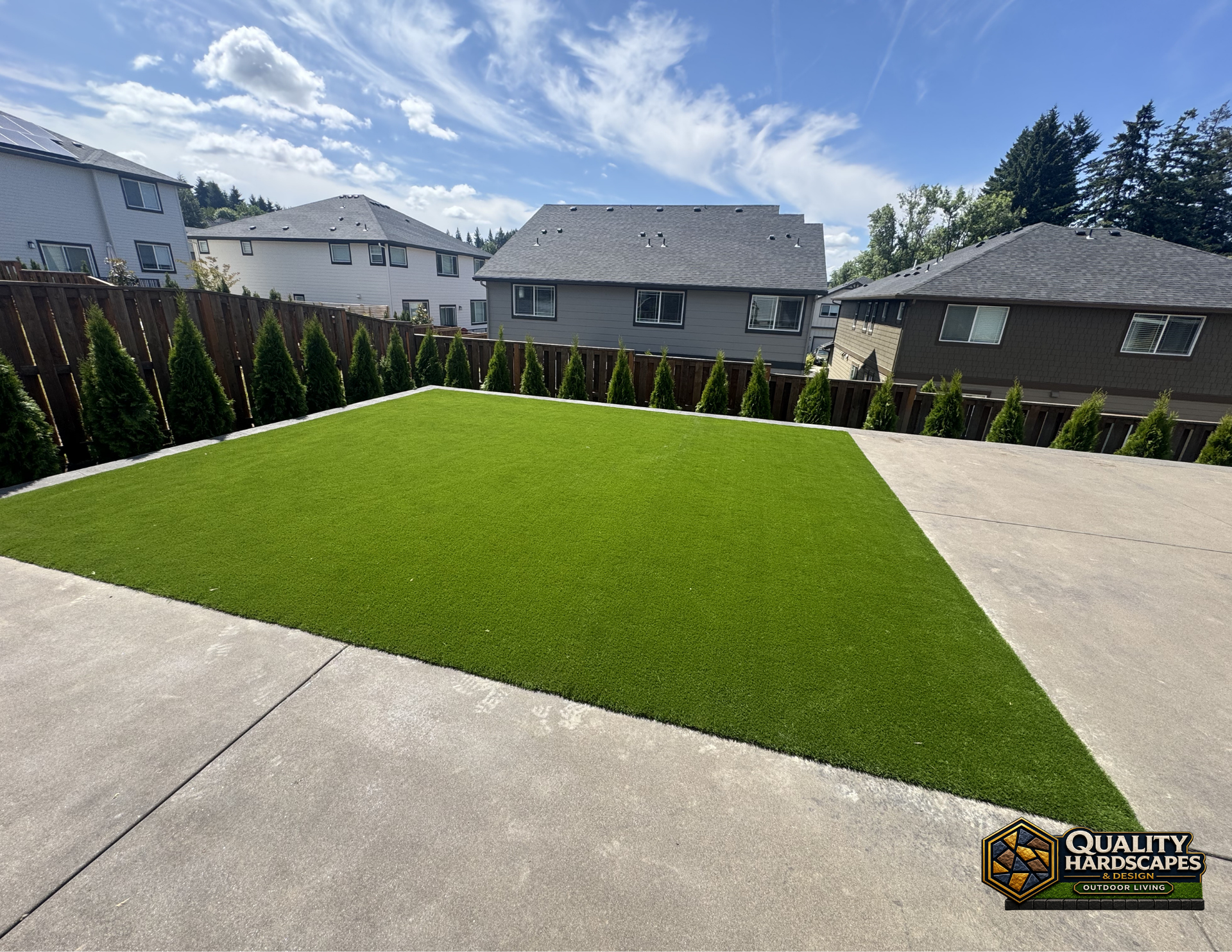 Freshly landscaped backyard with bright green sod, concrete patio, and neighboring houses under a blue sky