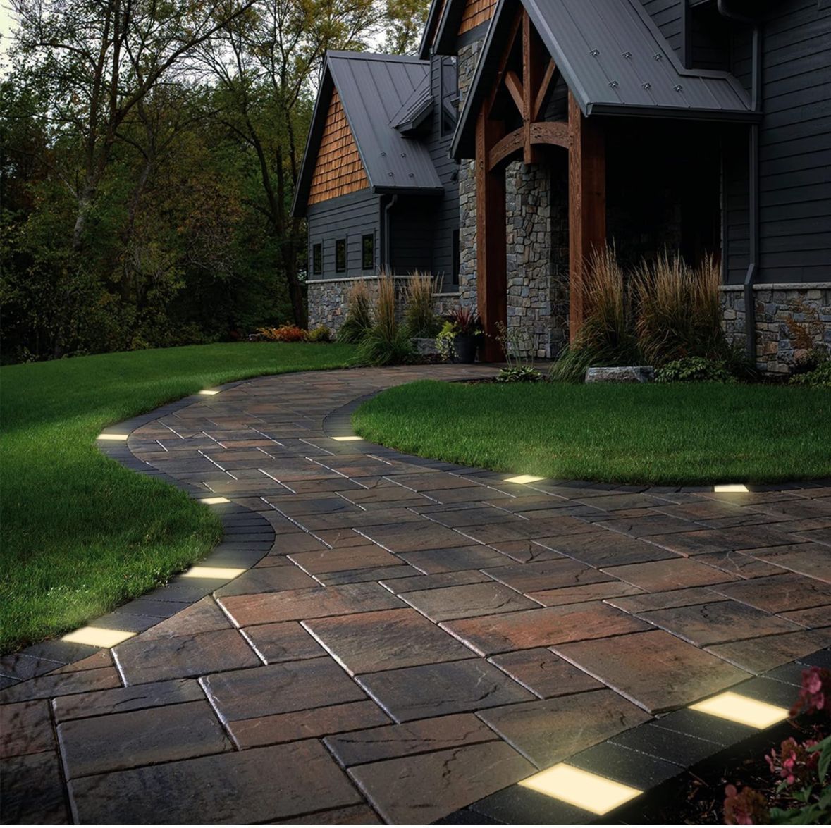 Pathway with embedded lights leading to a house with stone and wood accents.