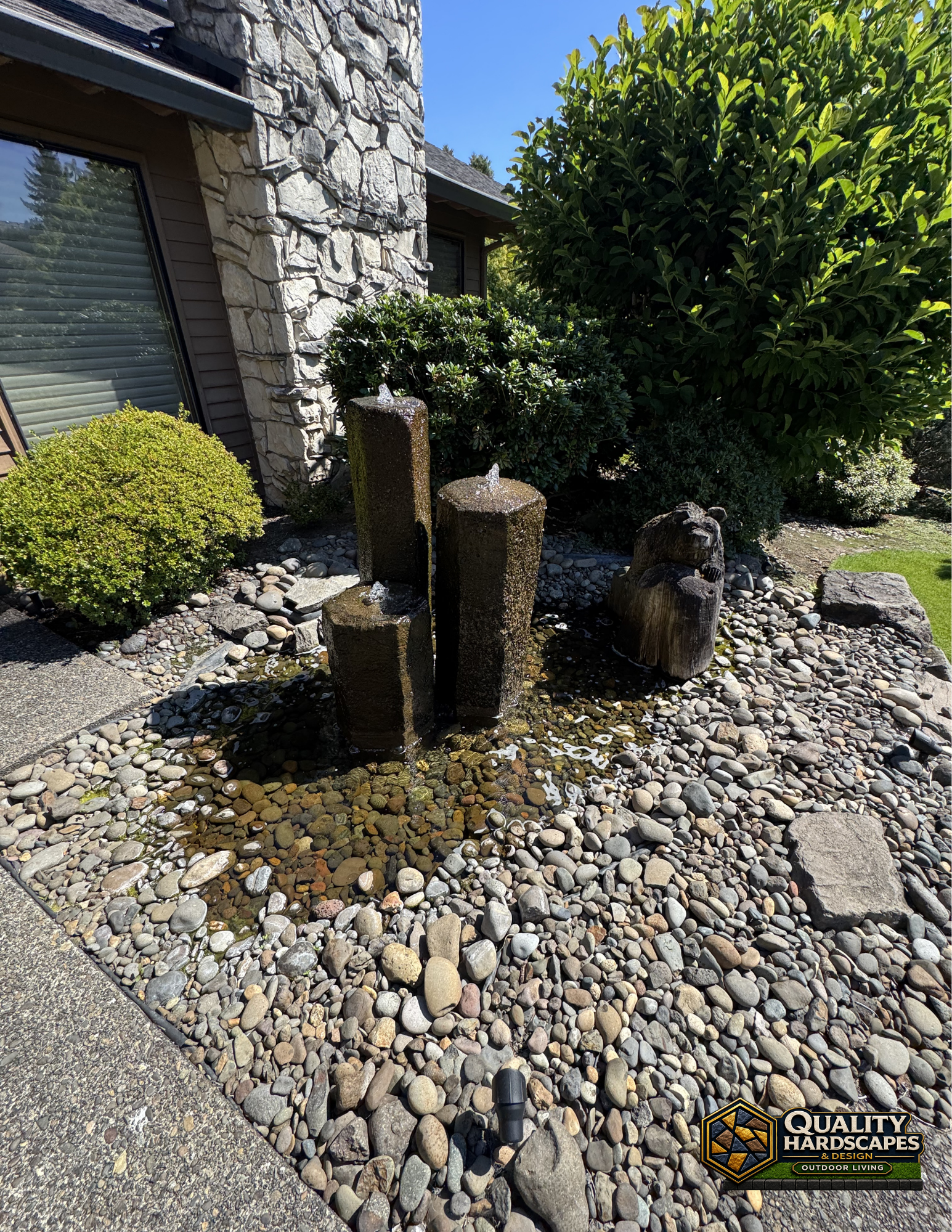 Three weathered stone fountain columns beside a garden pond with rocks and greenery