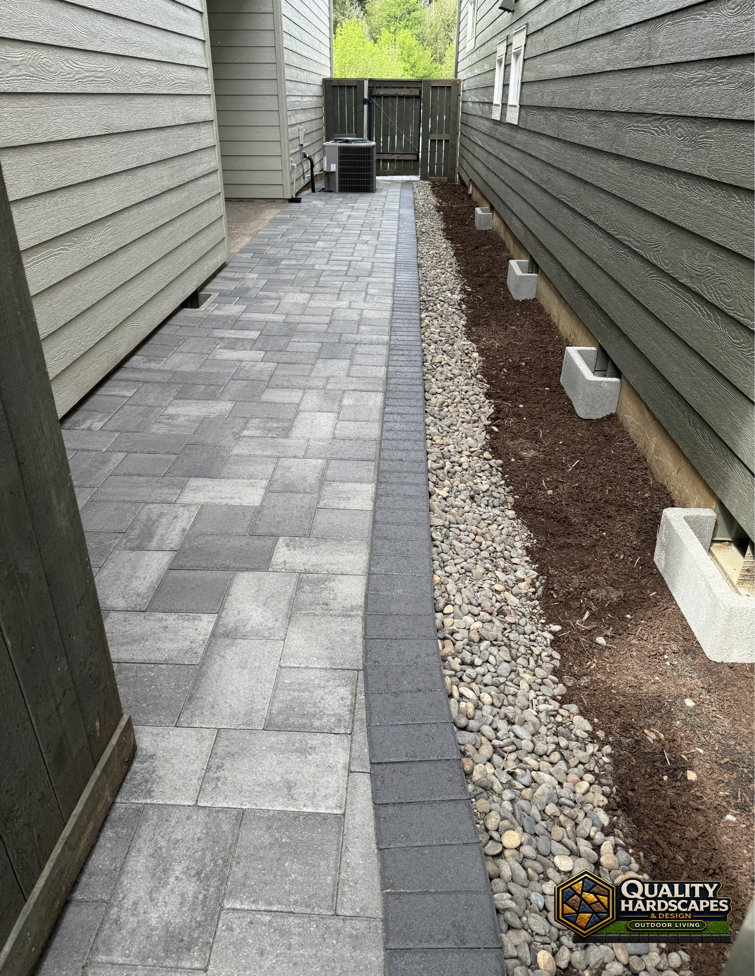 Narrow side yard with gray pavers, gravel strip, and house siding on both sides leading to a gate
