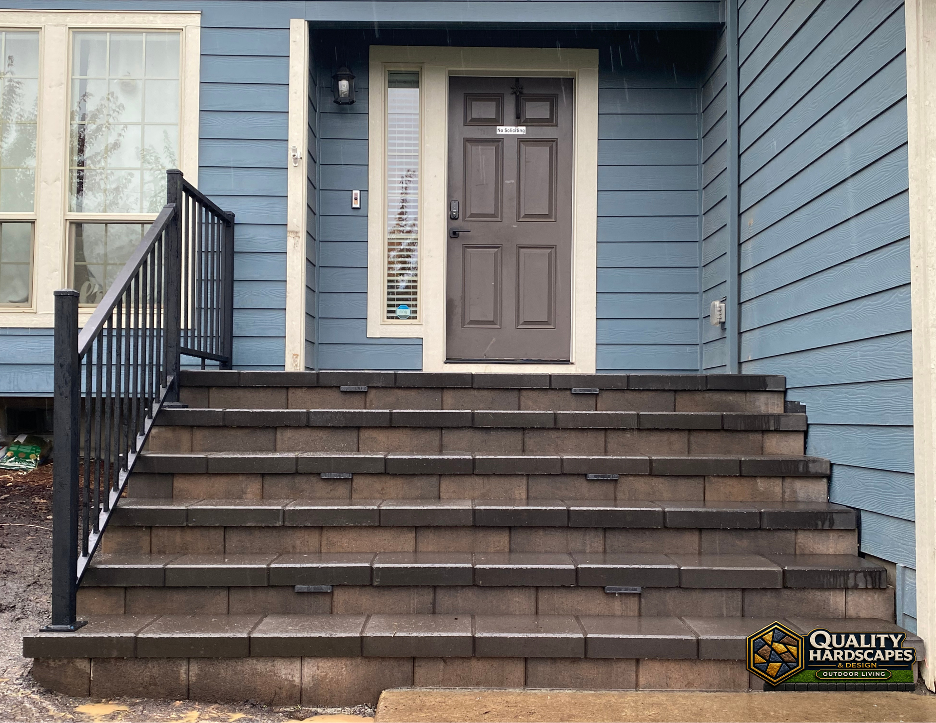 Front entry with brown front door, blue siding, and wide brick steps leading up from a walkway