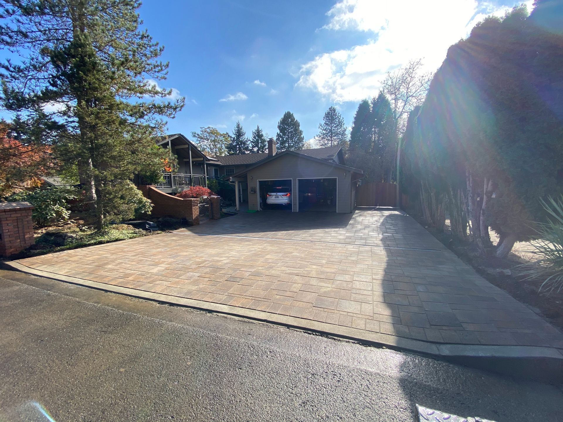 House with paved driveway; two-car garage; white car inside; trees and blue sky.