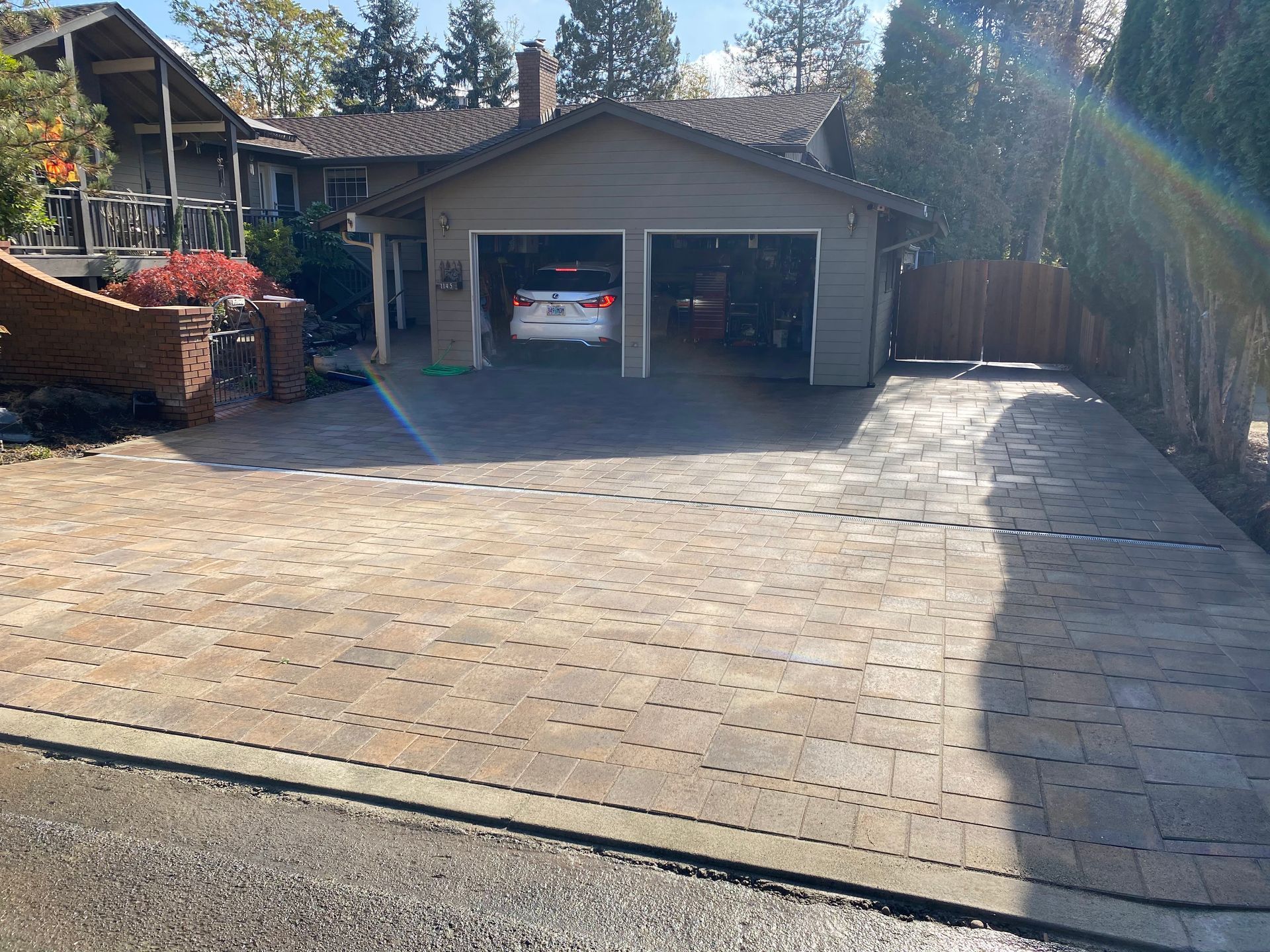 Brick paver driveway leads to a two-car garage with cars parked inside; house in the background.