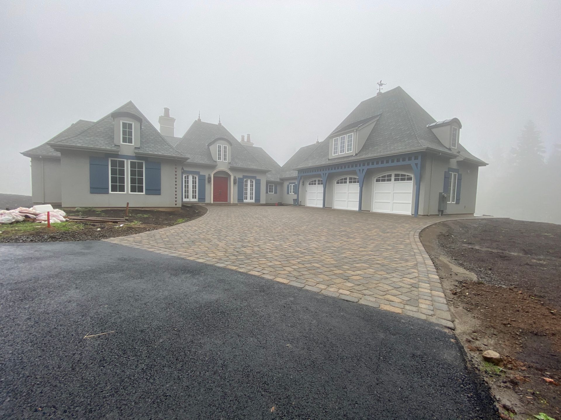 Gray house with stone driveway and three-car garage in foggy setting.