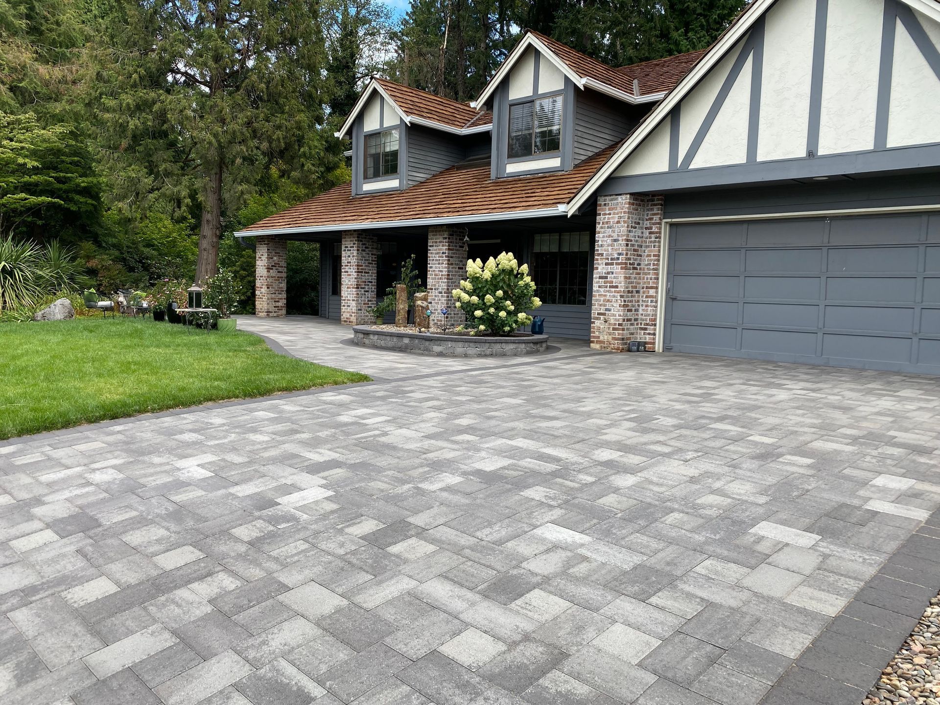 Driveway paved with gray and light gray bricks leads to a two-story house with a gray garage.