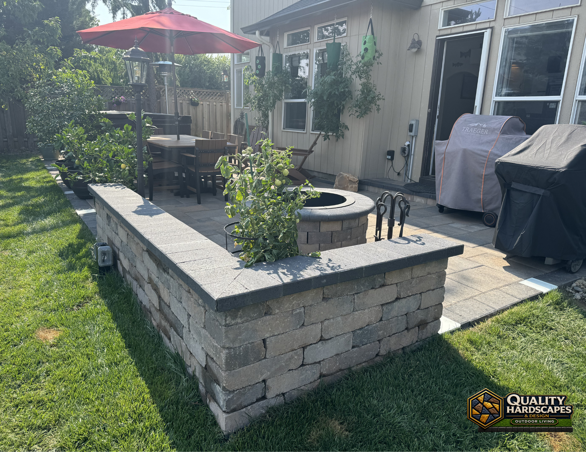 Backyard patio with stone fire pit, red umbrella, grill, and lawn beside a house
