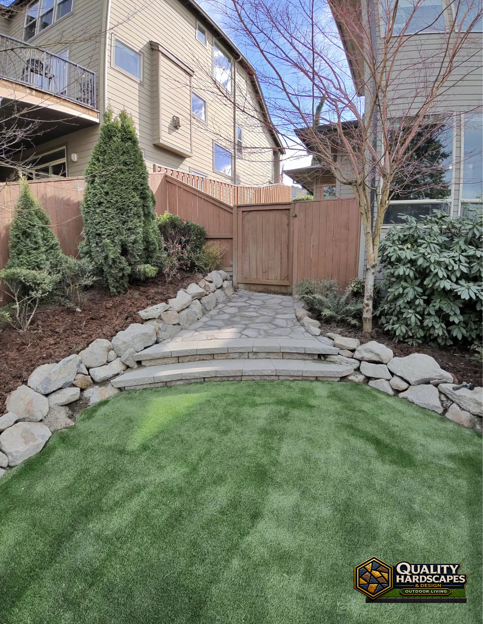 Landscaped backyard with stone steps, wooden gate, and green artificial turf between shrubs.