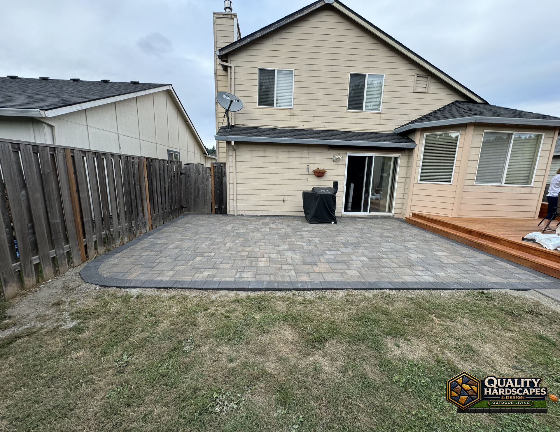 Backyard with gray patio pavers, beige house exterior, wooden fence, and small deck steps