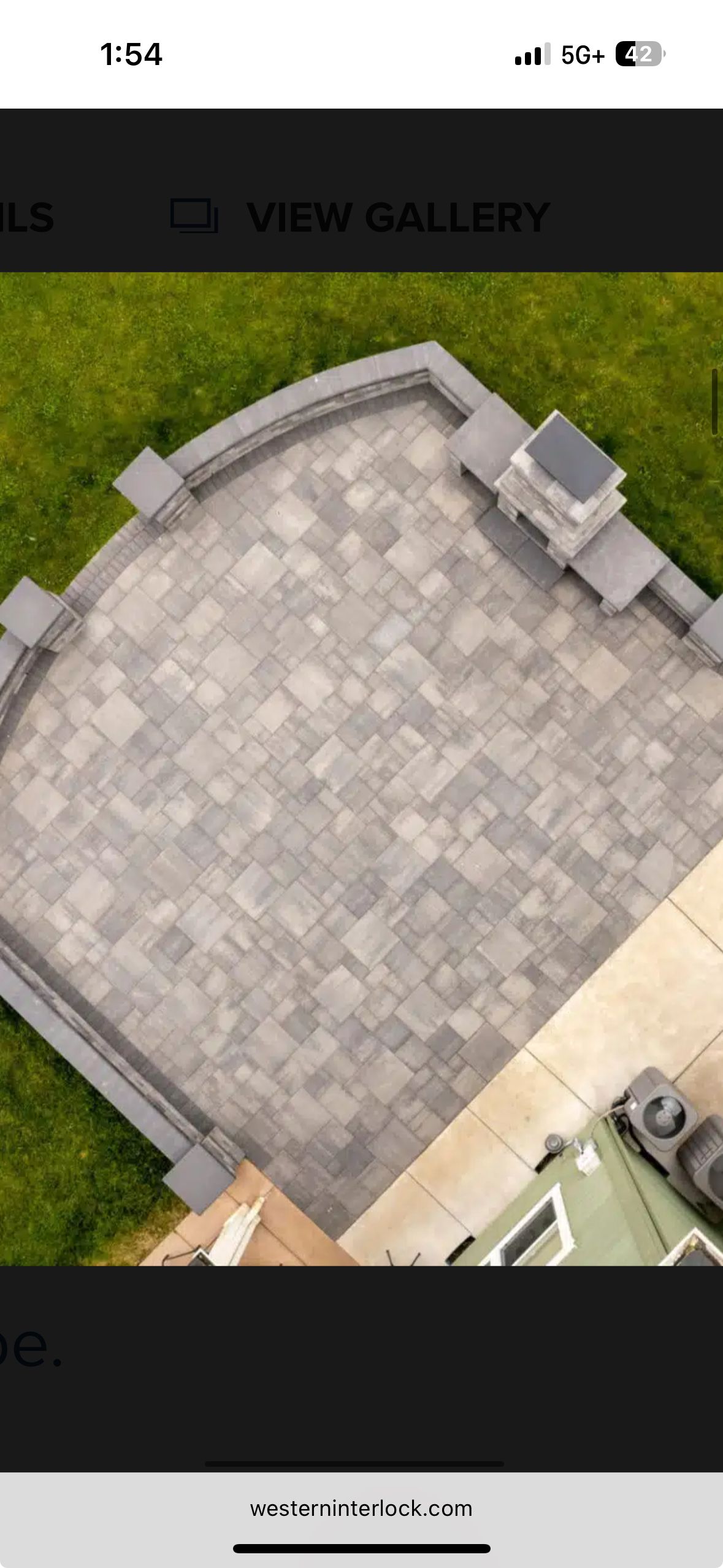 Overhead view of a gray paver patio with a curved wall, surrounded by grass, next to a building.