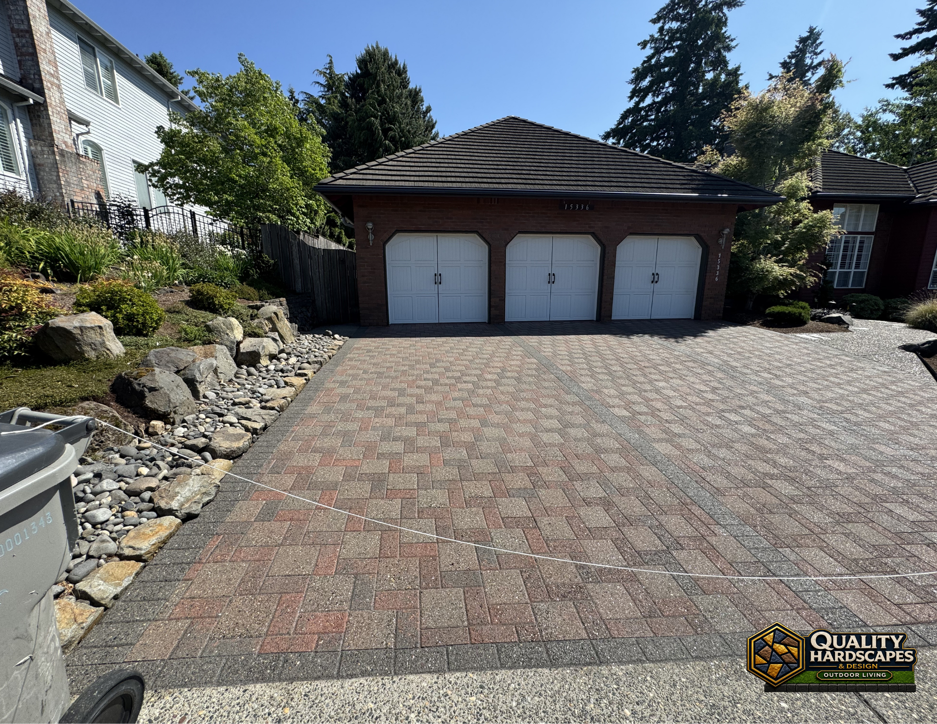 Brick-paver driveway leading to a three-car garage with white doors and landscaping on the left