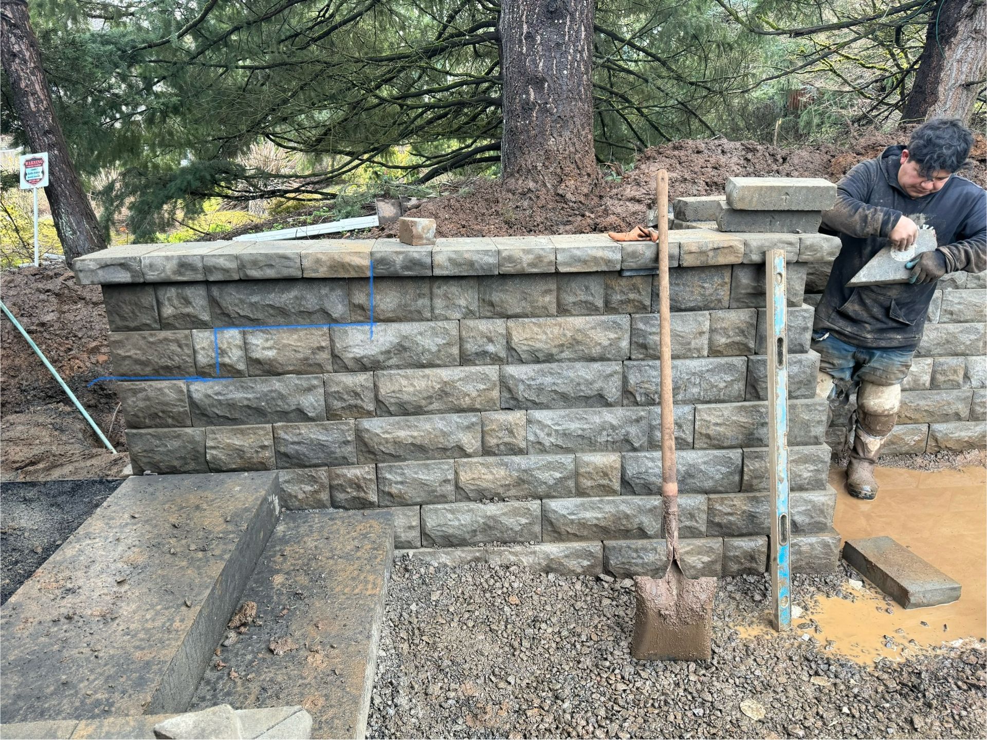 Construction worker building a stone retaining wall outdoors, using tools.