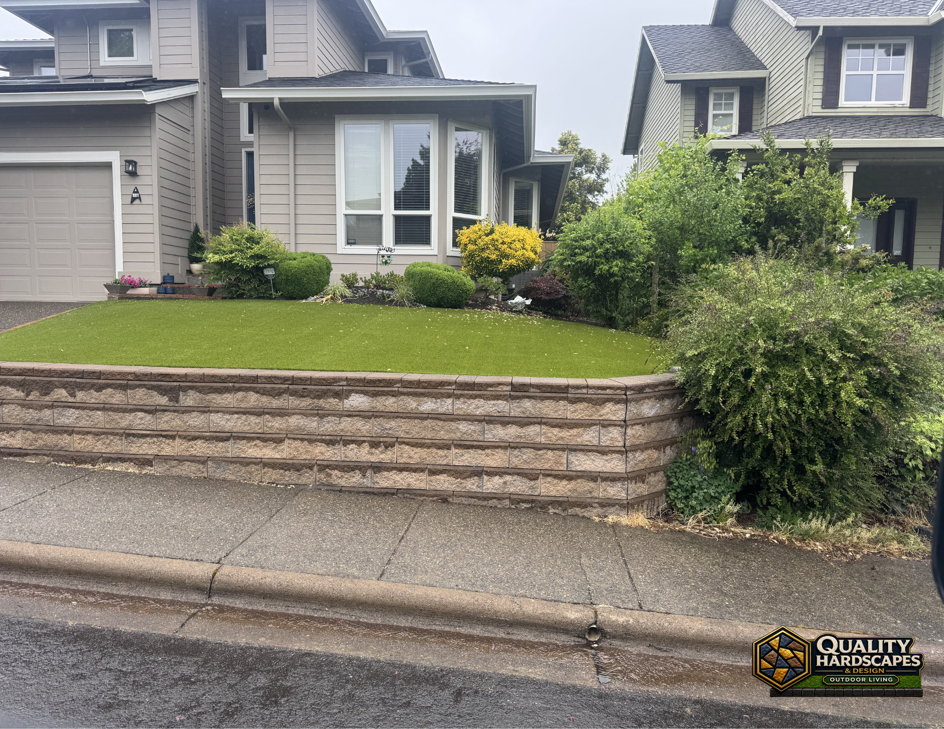Suburban house with a terraced stone retaining wall and green lawn beside the street