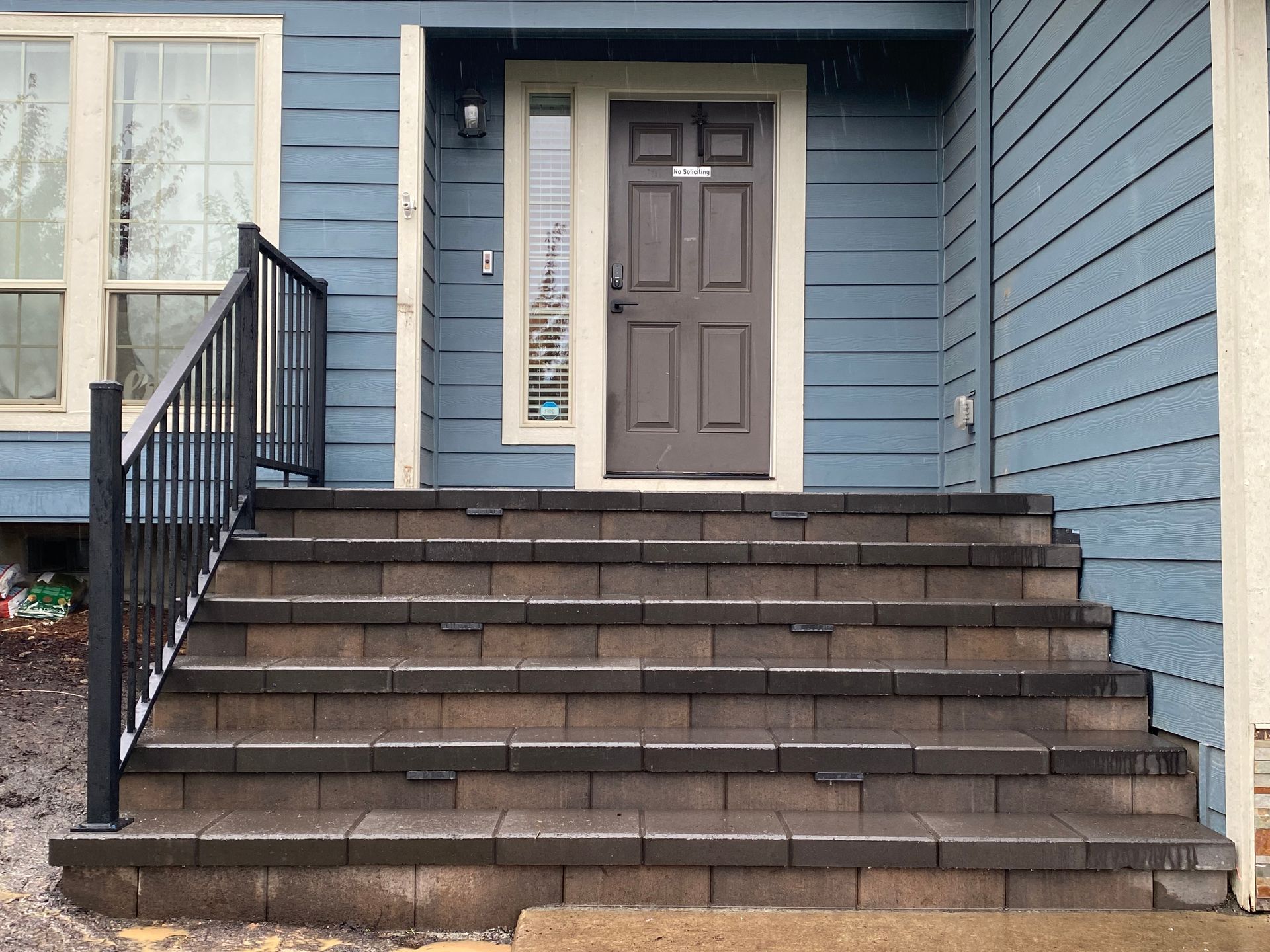 Exterior of a house with steps leading to a brown door. Black railing, blue siding.