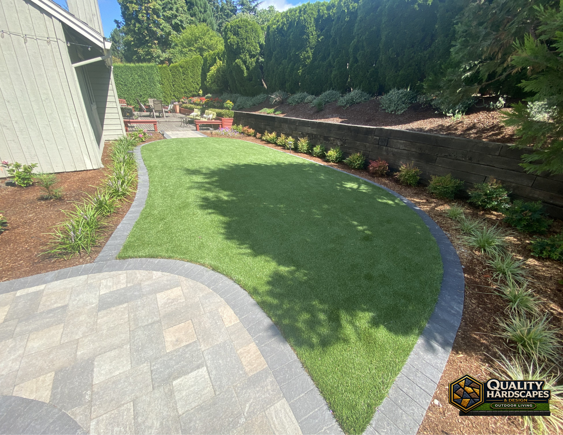 Curved green lawn bordered by pavers, mulch beds, and shrubs beside a house in a landscaped yard