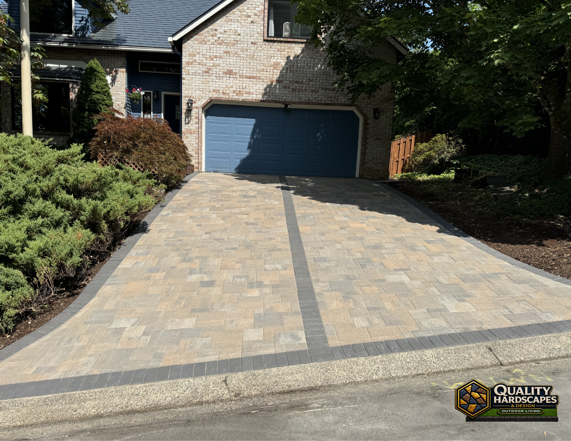 Stone driveway leading to a blue garage door beside a brick house, bordered by landscaping.