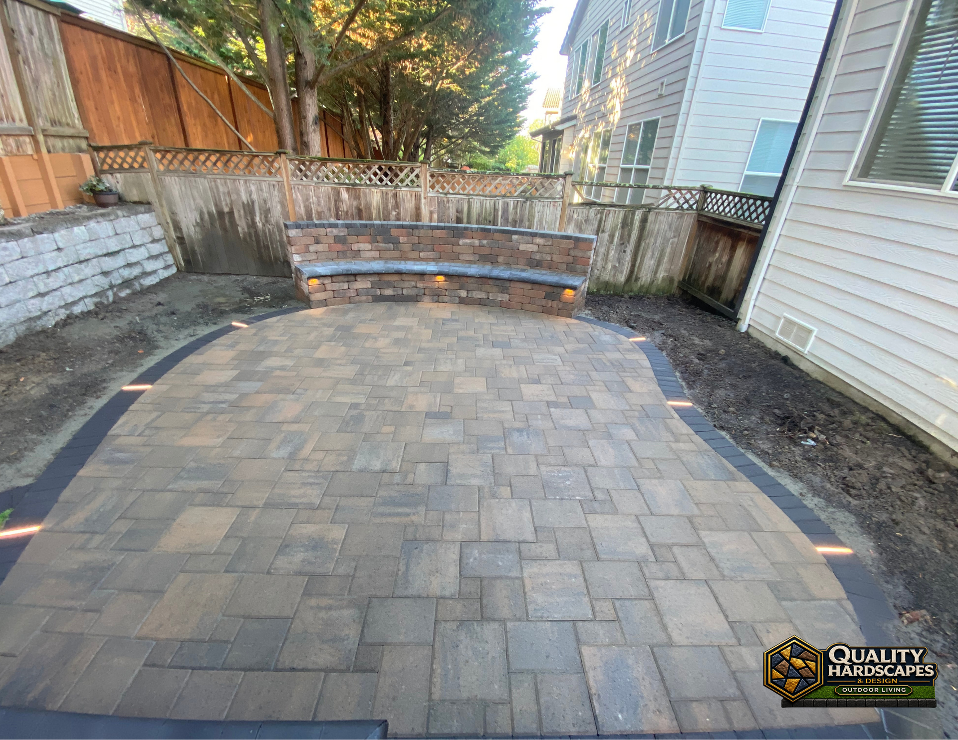 Paver patio with curved stone steps and wood fence in a narrow backyard