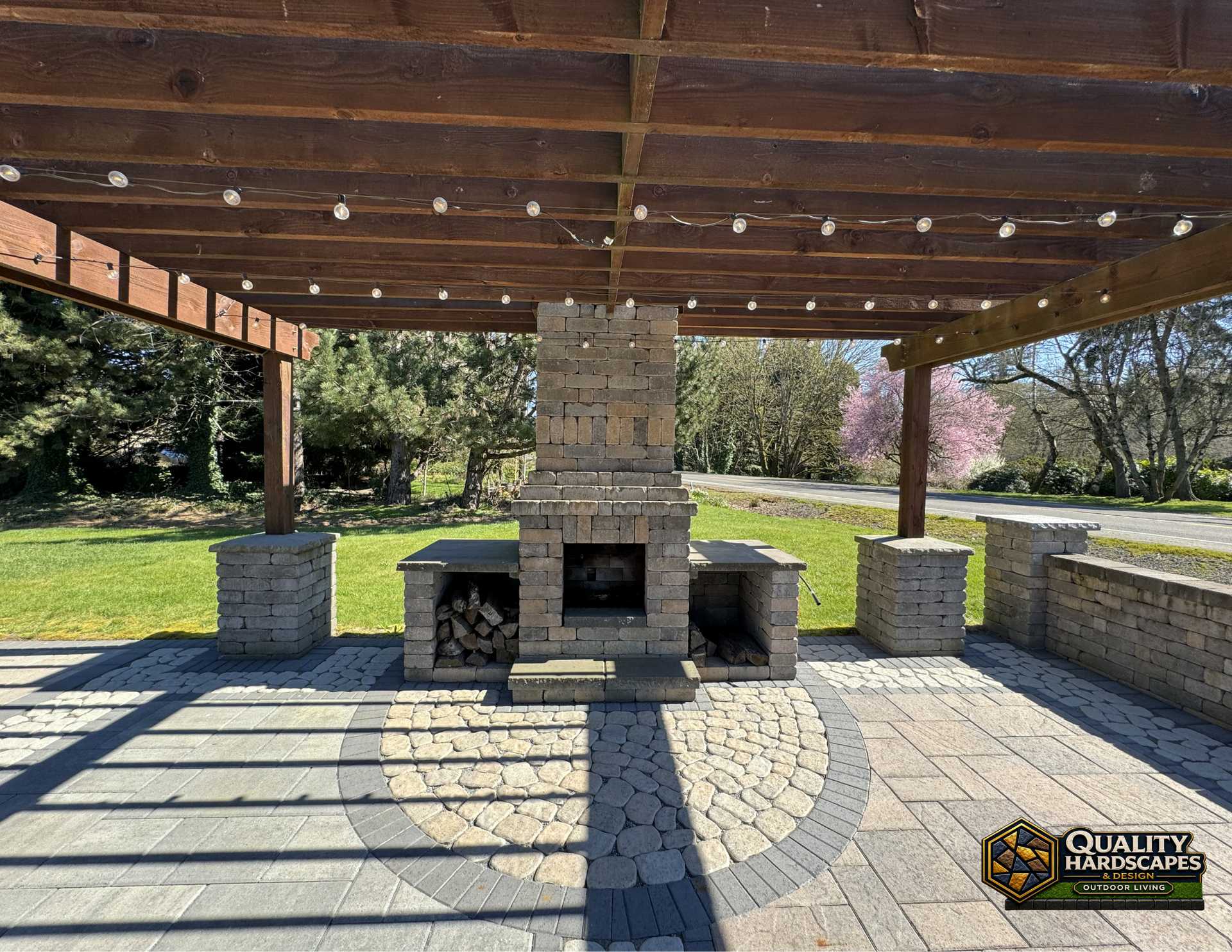 Outdoor stone fireplace under a wooden pavilion with picnic tables in a park