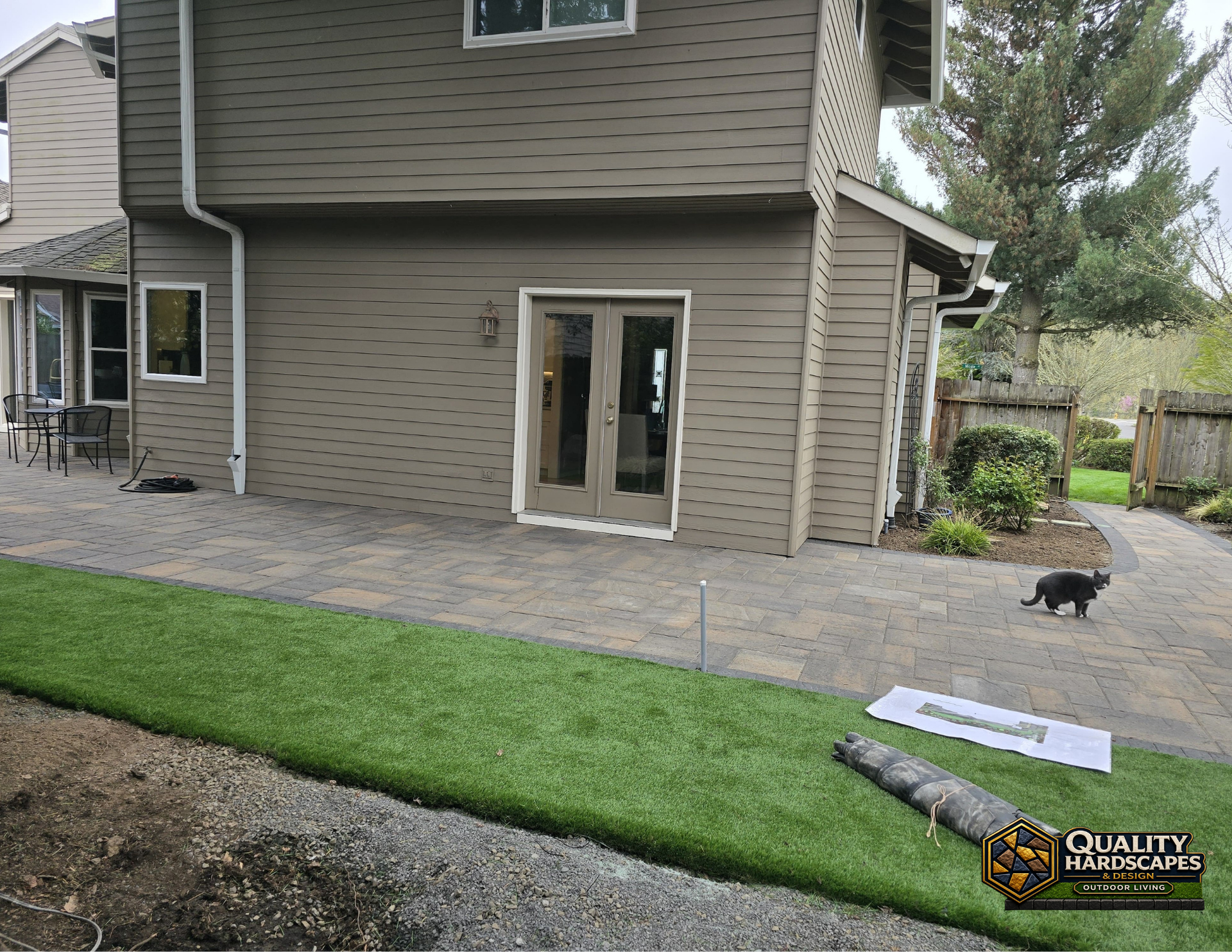 Backyard patio and stone walkway beside a house, with a small dog on the pavers.
