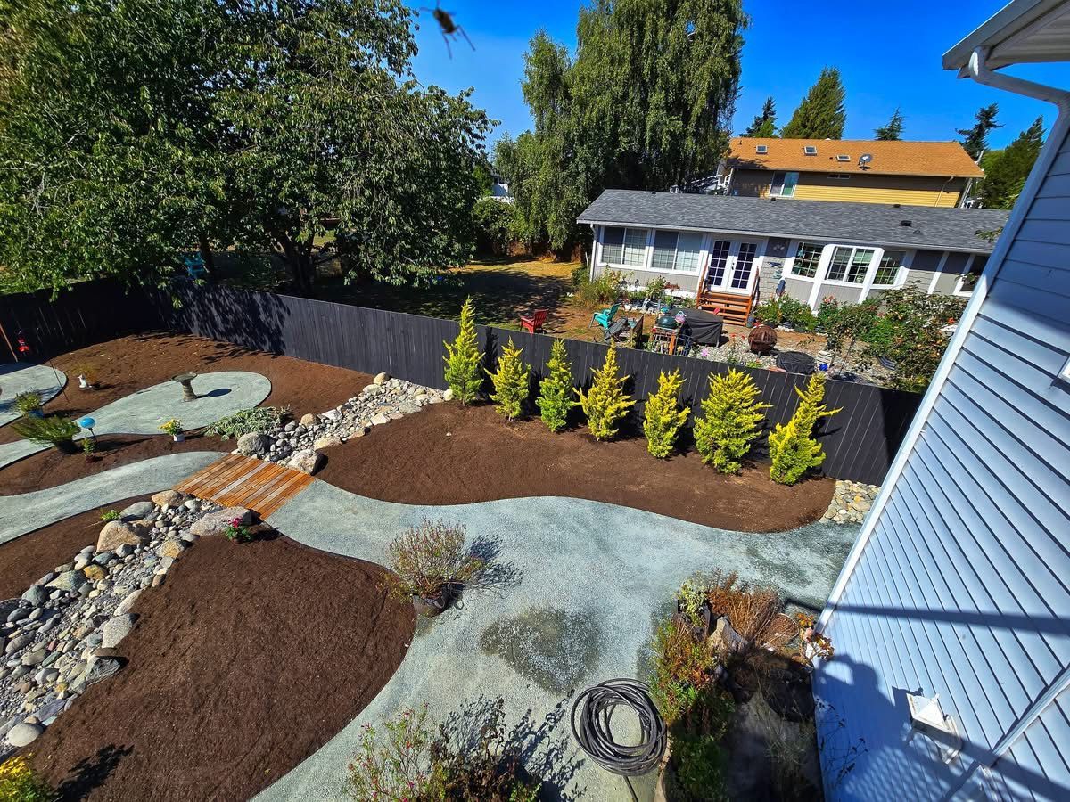 Backyard landscaping with mulch, gravel paths, rock features, and small trees along a black fence.