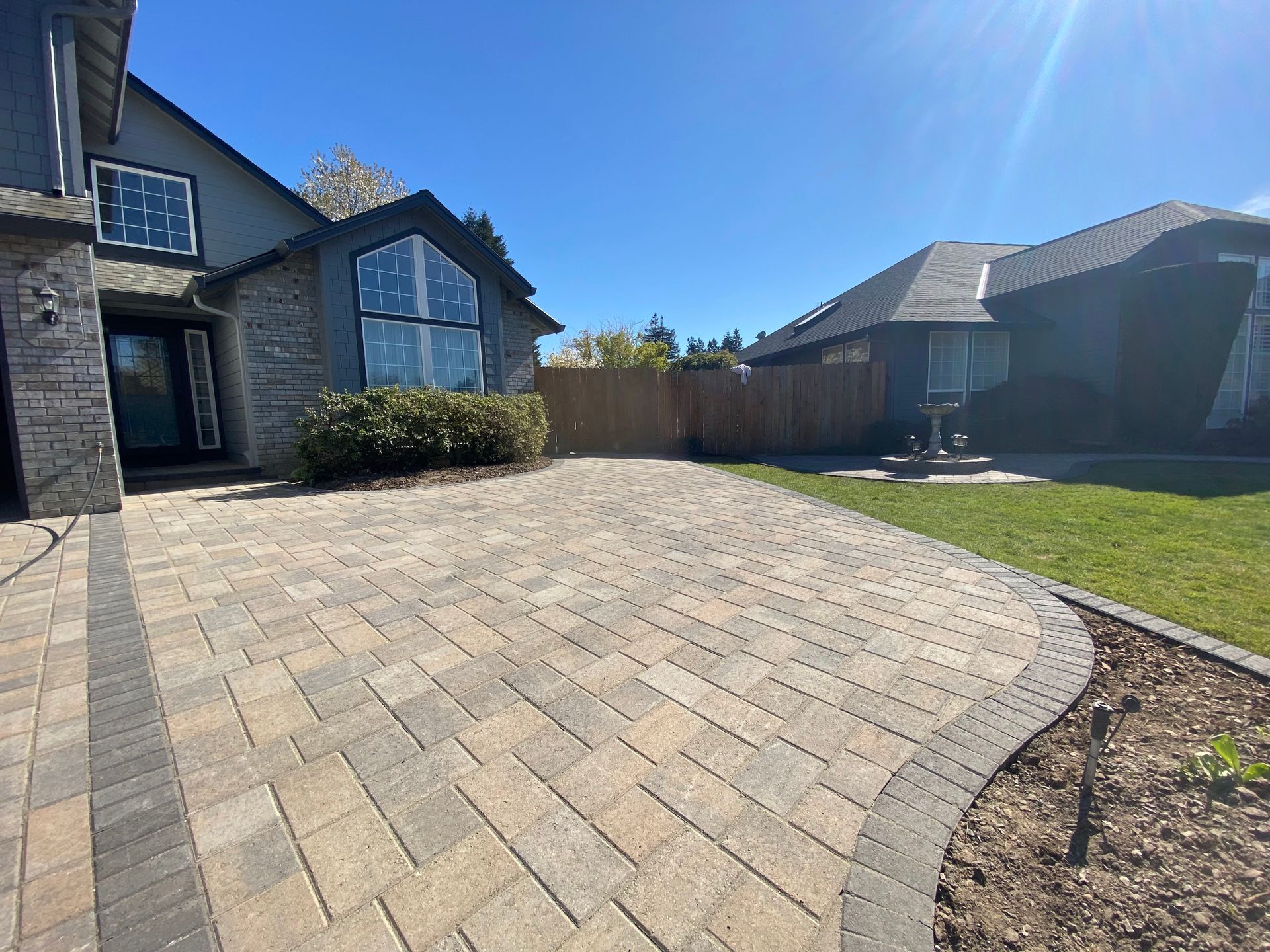 A paved driveway leads to a stone-clad house under a bright blue sky.