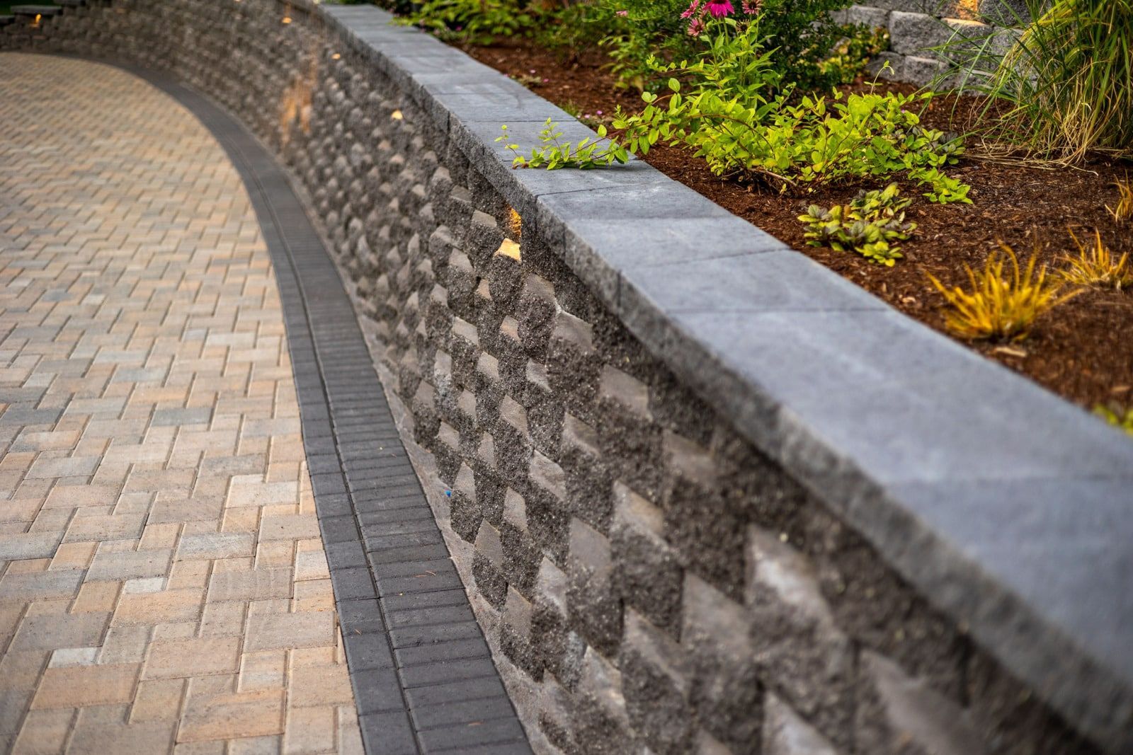 Stone retaining wall with a paved walkway curving around it. Brown and grey tones.