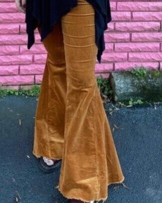 A woman wearing flared pants is standing in front of a pink brick wall.