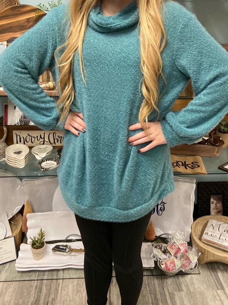 A woman wearing a blue sweater and black pants is standing with her hands on her hips.