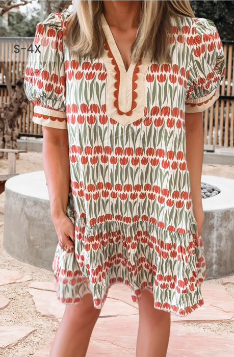 Woman in a tulip-print dress outdoors. The dress is red and white with cream trim. She is smiling.