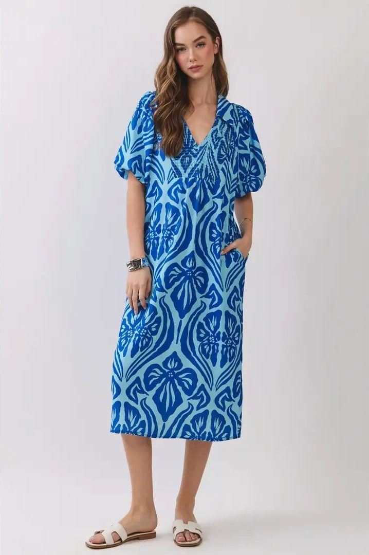 Woman wearing a blue patterned midi dress and sandals, standing against a plain light background