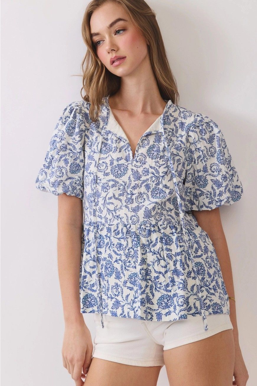 Woman wearing a blue floral blouse and white shorts against a light background