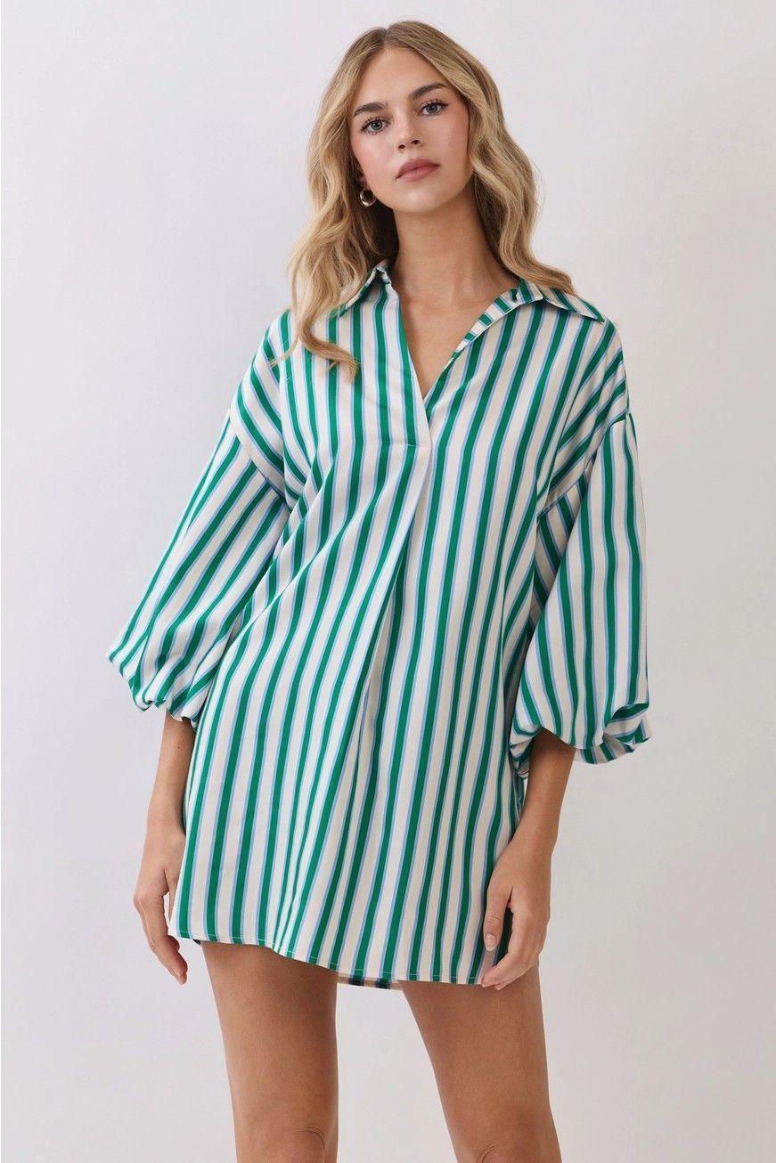 Woman wearing a green-and-white striped oversized shirt dress against a plain background