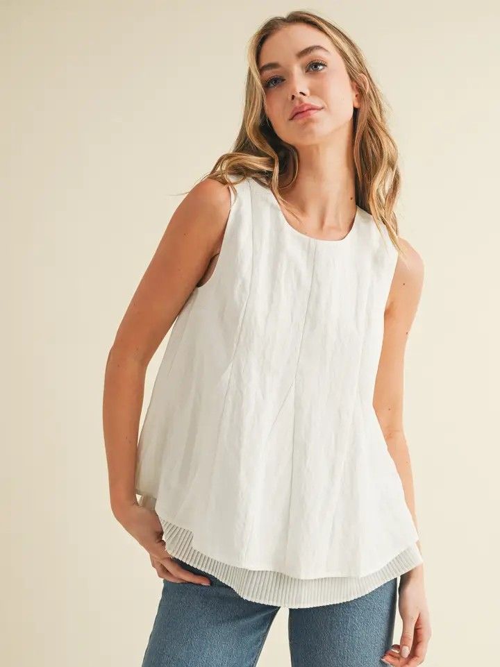 Woman in a white sleeveless top and jeans posing against a beige background