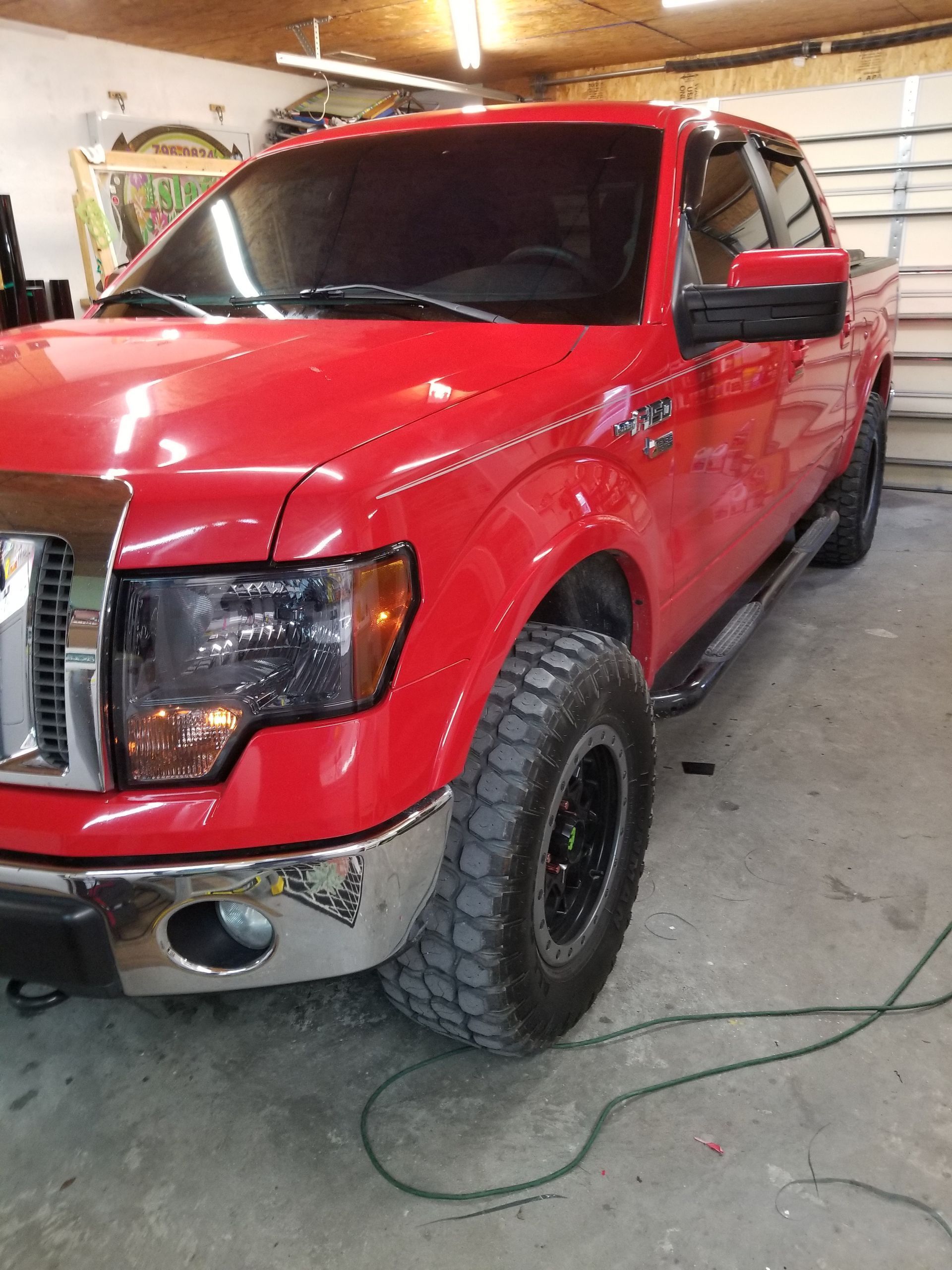Red Ford F-150 truck with tinted windows, black wheels, and off-road tires, parked inside a garage.