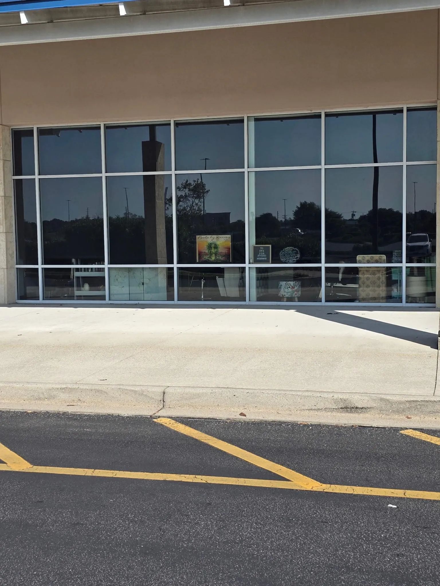 Storefront with large windows, tan building, paved area, yellow parking lines.