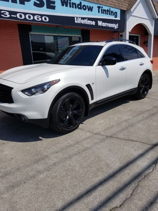 White SUV with black wheels parked in front of a window tinting business.