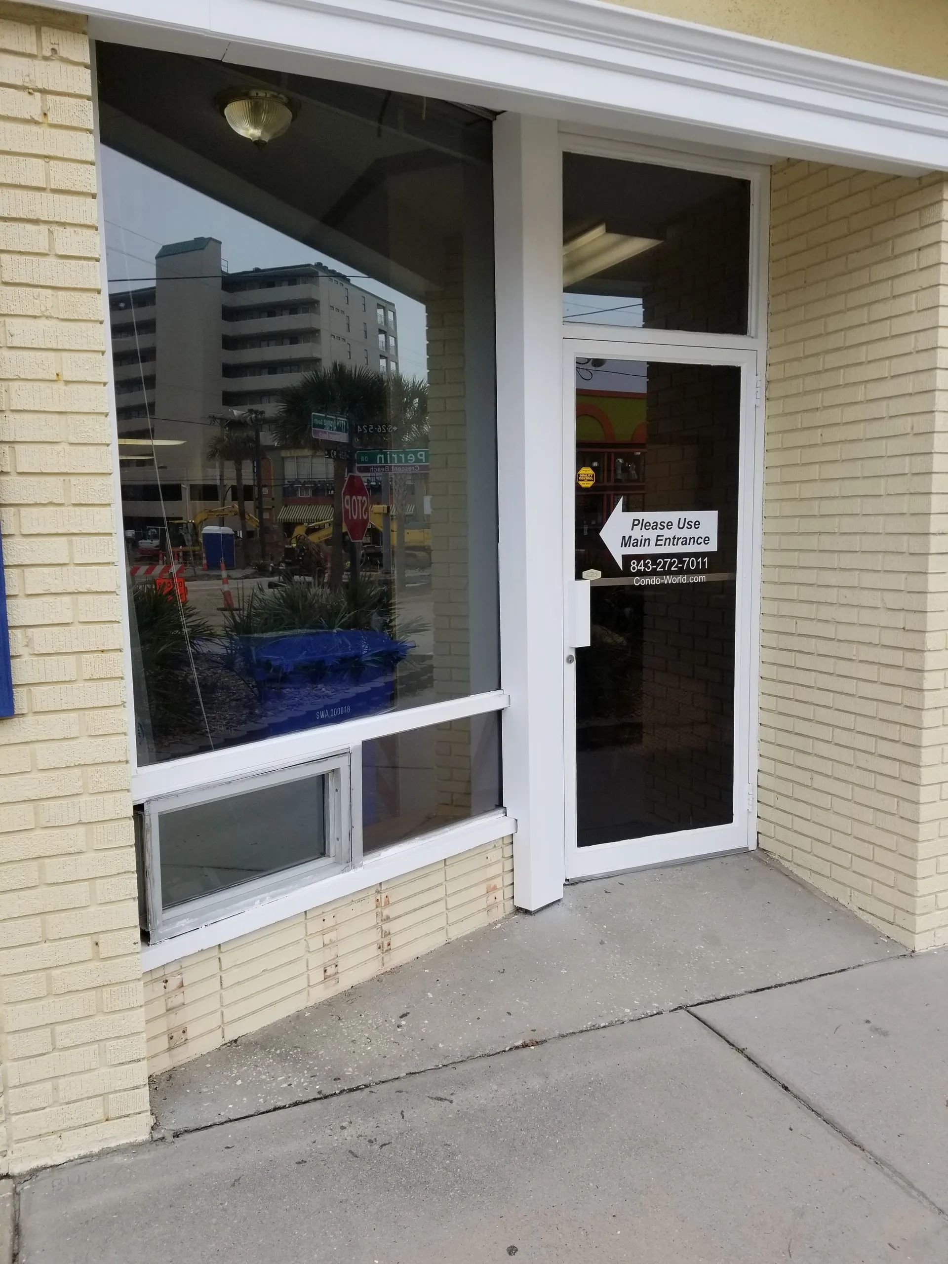 Exterior view of a commercial building with a glass door and window. Beige brick and concrete.