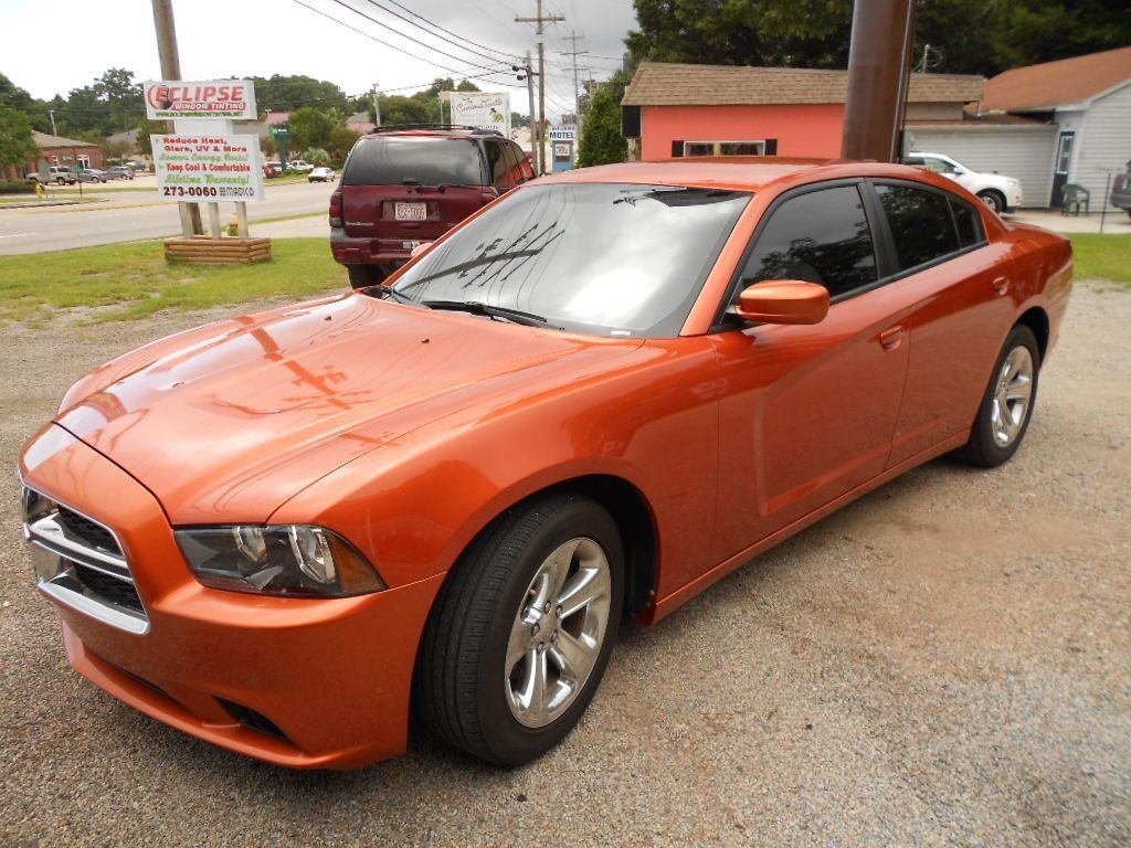 Orange Dodge Charger parked on gravel, in front of a storefront.