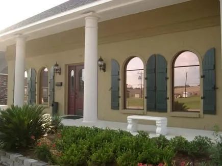 Tan building with white pillars, green shutters, arched windows, and a bench.