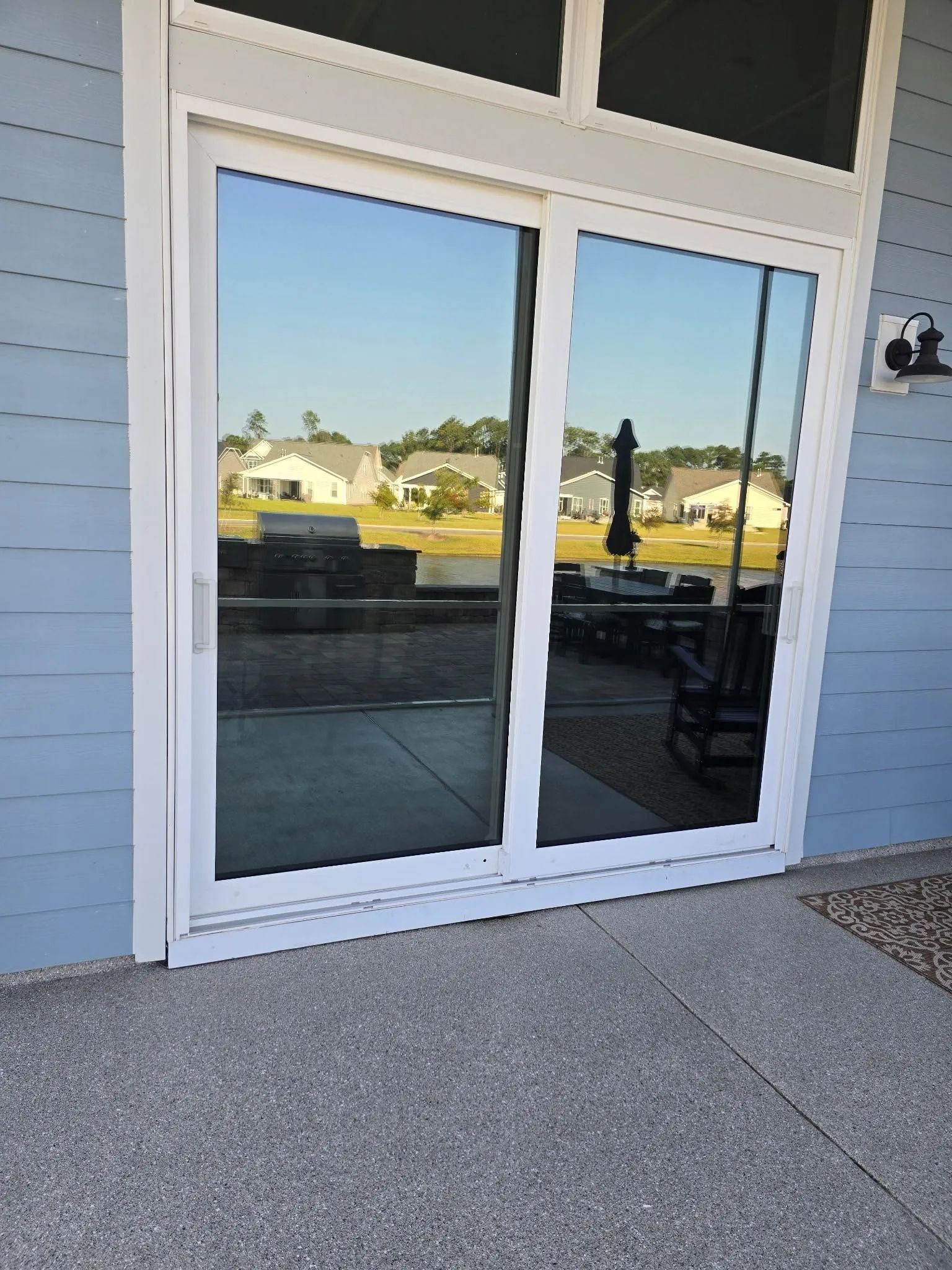 Sliding glass doors reflecting a sunny outdoor scene, framed in white, on a light blue exterior wall.