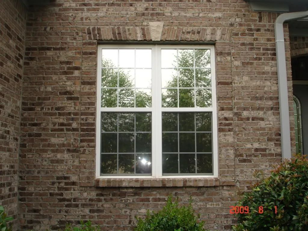 Brick exterior with a white-framed window reflecting trees and sky.